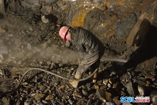 在赶羊沟隧道左洞内，一位建设者在坚硬的岩石上打洞准备埋放炸药。由于汶马高速的地质结构非常复杂，给开挖隧道带来非常大的难度。